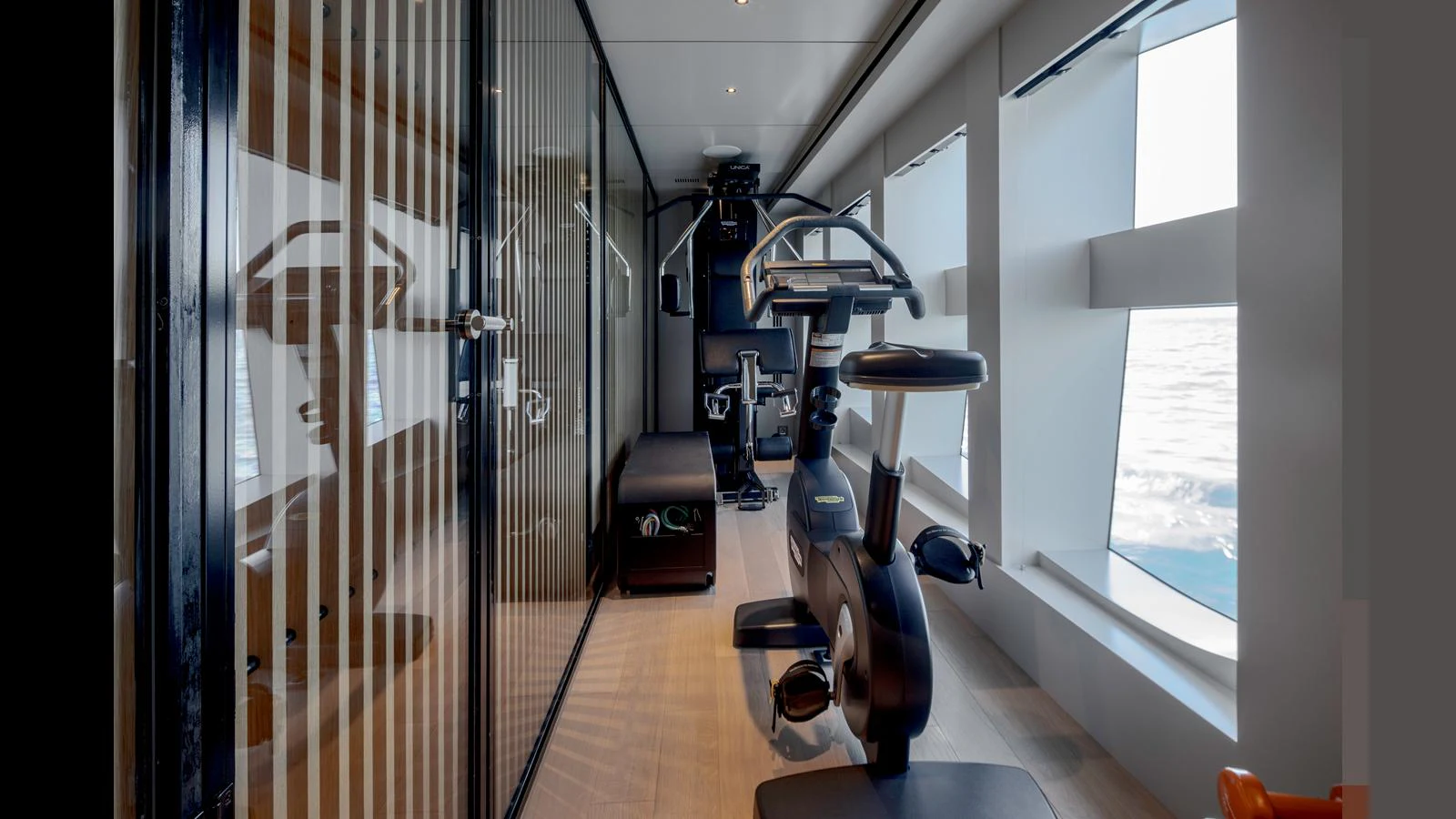 The yacht features a well-equipped gym with modern exercise equipment and large windows offering ocean views. aboard Q.M Yacht for Sale