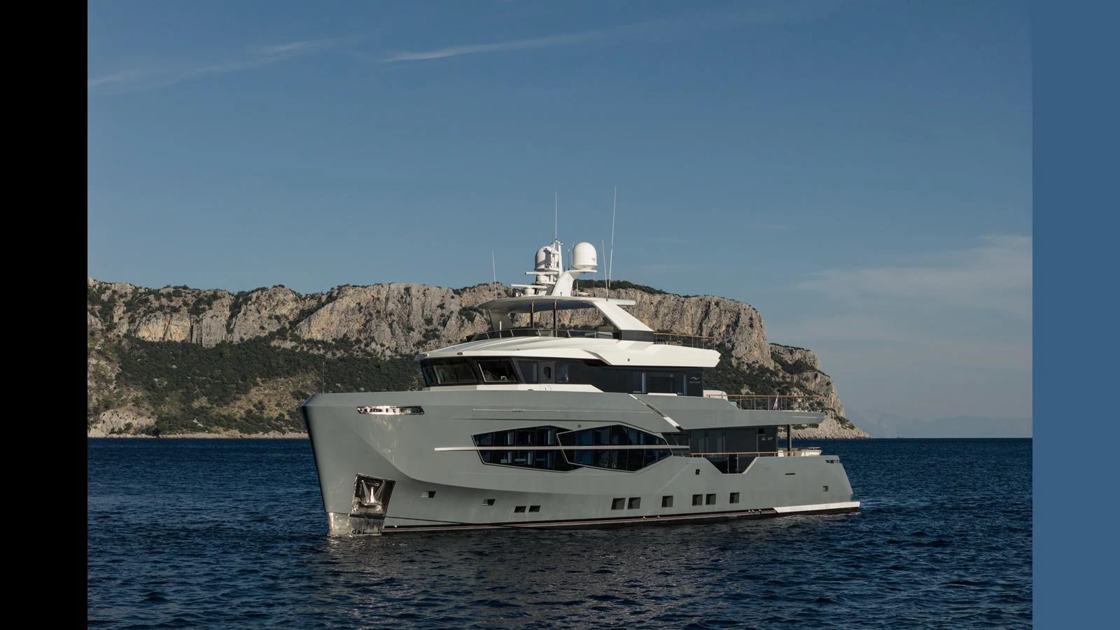 A sleek and modern yacht cruising on calm waters with a scenic rocky coastline in the background. aboard Q.M Yacht for Sale