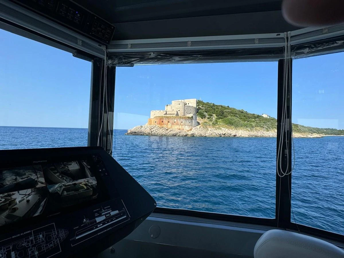The helm station offers a stunning view of a historic coastal fortress through large windows. aboard D&D Yacht for Sale