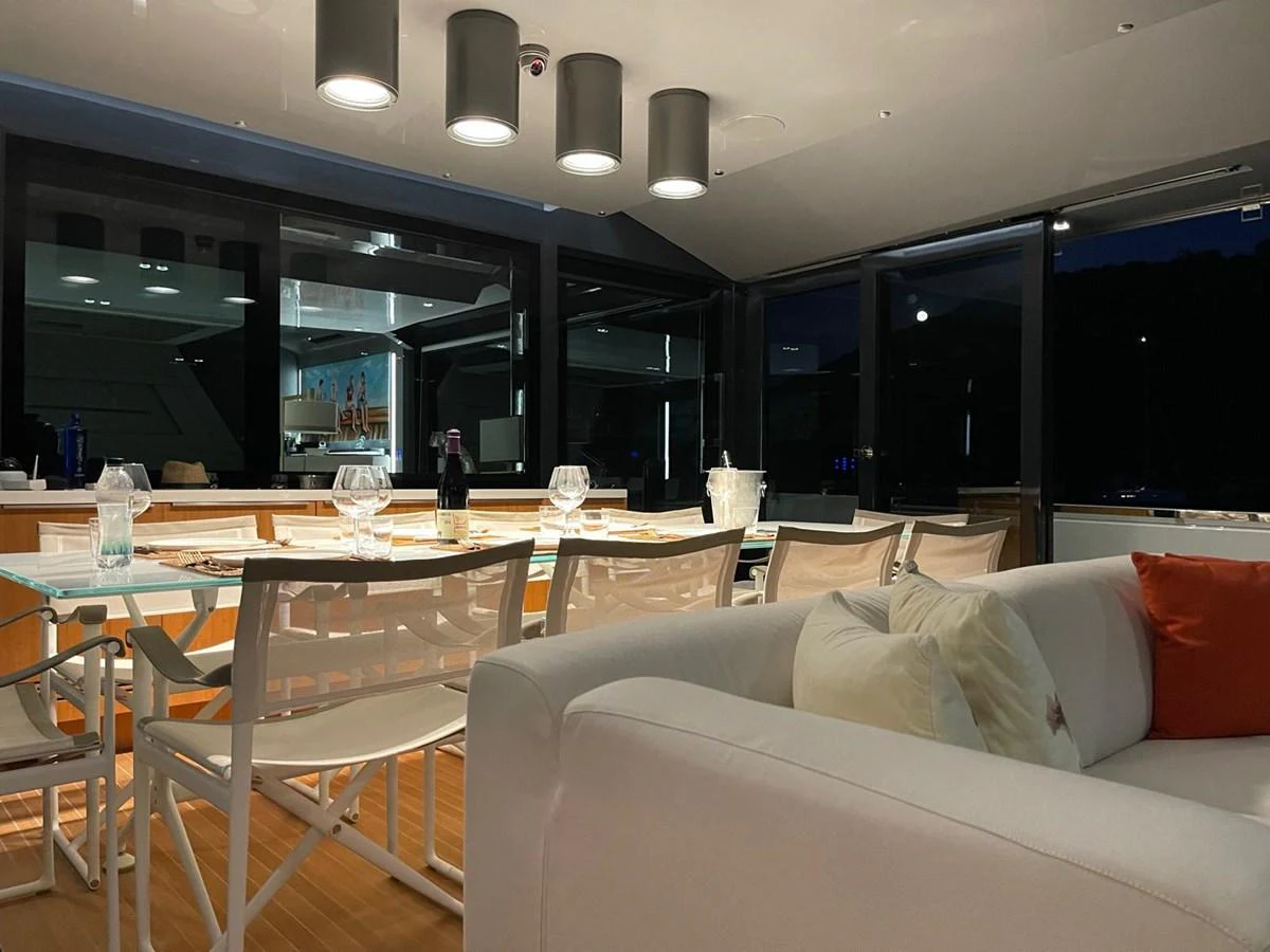 The yacht's dining area features a modern table with comfortable seating, set against large windows offering a view of the night sky. aboard D&D Yacht for Sale
