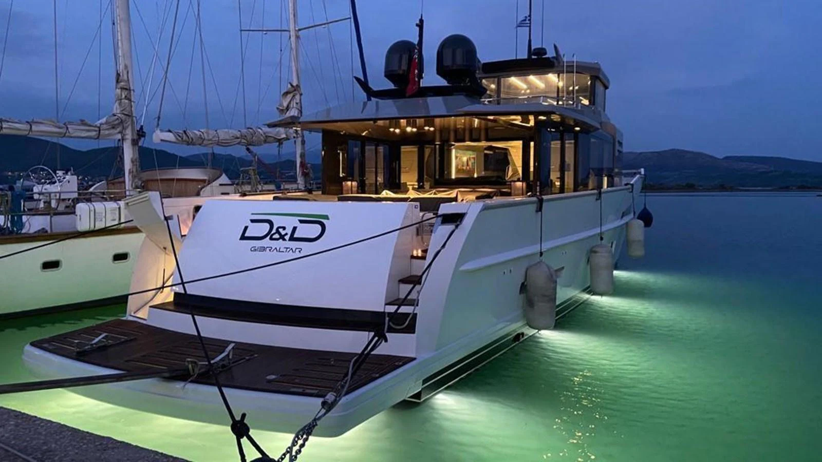 The yacht is docked at twilight, showcasing its illuminated aft deck and sleek design. aboard D&D Yacht for Sale