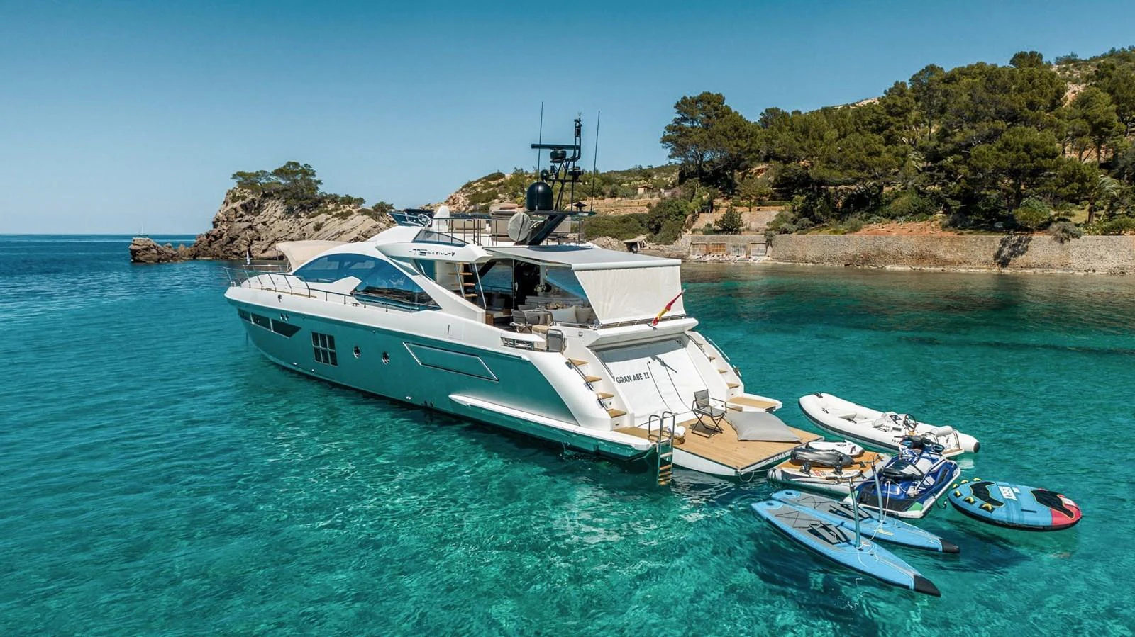 A sleek yacht is anchored in a serene, turquoise bay with various water toys ready for use. aboard GRAN ABE II Yacht for Sale