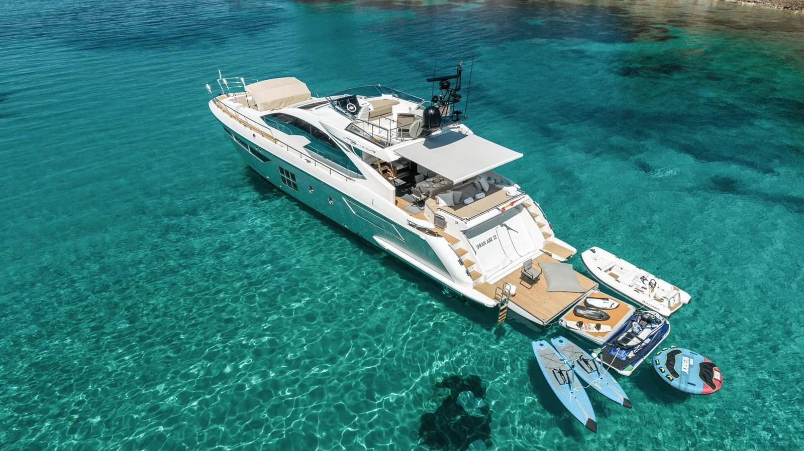 A luxurious yacht anchored in crystal-clear waters, showcasing its spacious aft deck and water toys. aboard GRAN ABE II Yacht for Sale