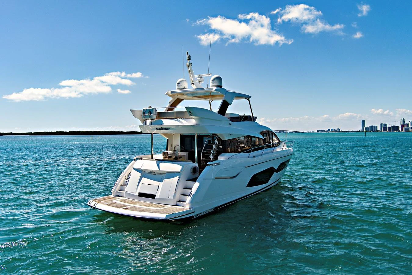 A sleek and modern yacht cruising on calm blue waters with a cityscape in the background. aboard SMITTEN Yacht for Sale