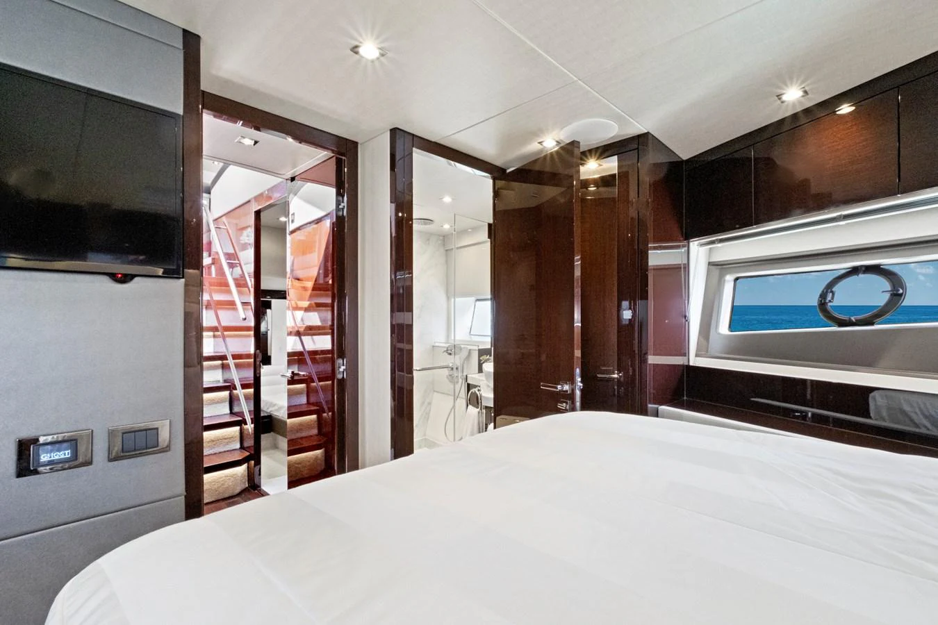 The stateroom features a luxurious bed, modern fixtures, and a view of the sea through a large window. aboard SMITTEN Yacht for Sale