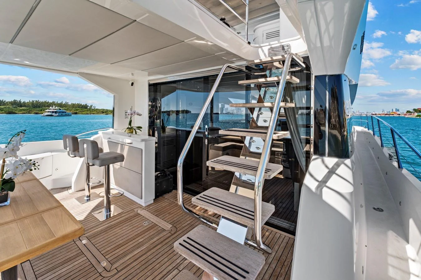 The aft deck features a stylish staircase, bar seating, and a beautiful view of the water. aboard SMITTEN Yacht for Sale