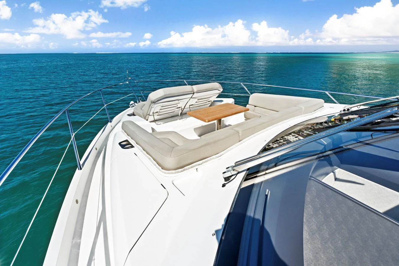 The foredeck features a luxurious sunbathing area with plush seating and a wooden table, offering stunning ocean views. aboard SMITTEN Yacht for Sale