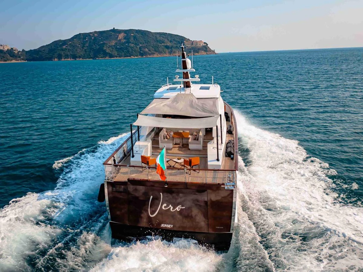 The yacht cruises smoothly through the water, showcasing its elegant aft deck with comfortable seating and a shaded area. aboard VERO Yacht for Sale