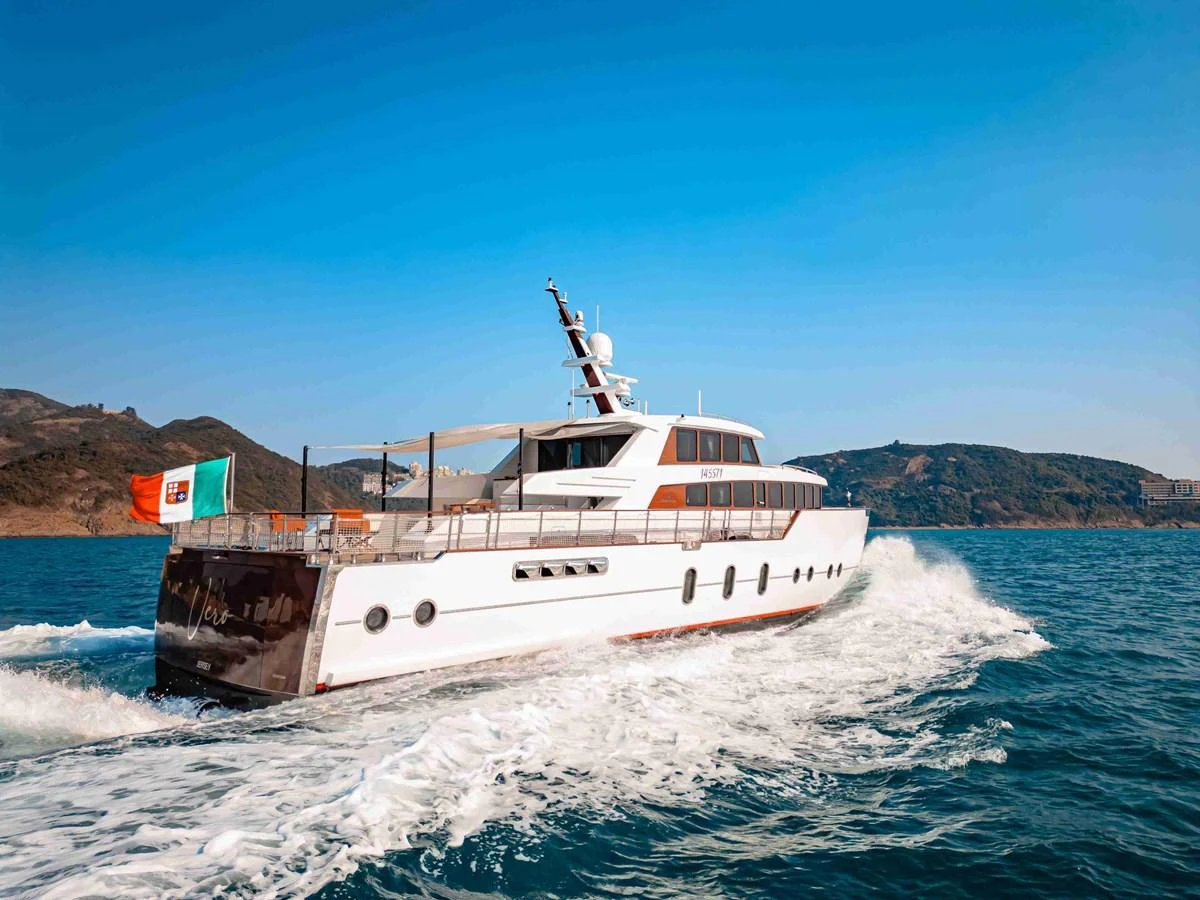 A sleek yacht glides through the water against a backdrop of scenic hills. aboard VERO Yacht for Sale