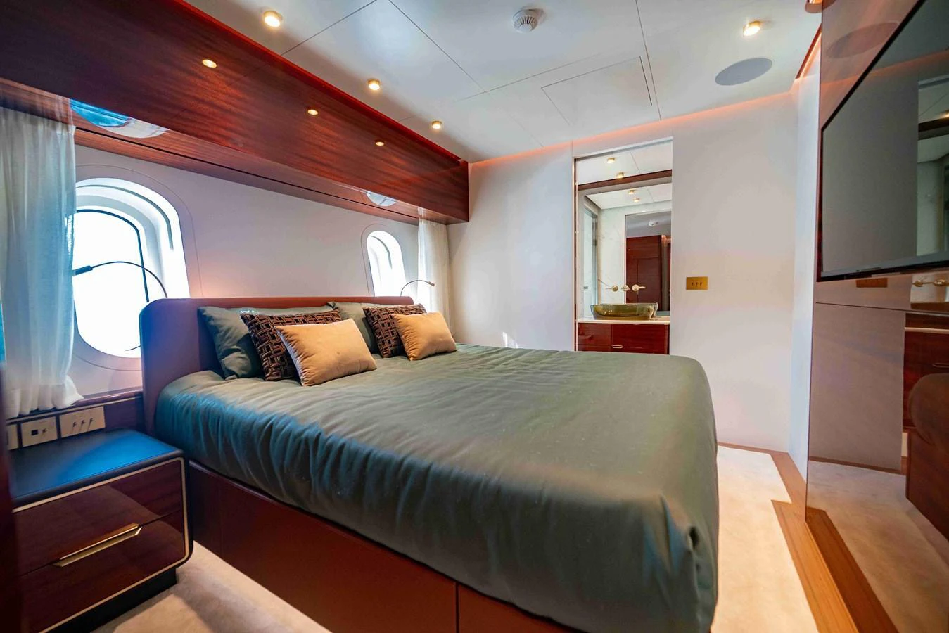The stateroom features a plush bed with elegant wood finishes and ample natural light from the windows. aboard VERO Yacht for Sale