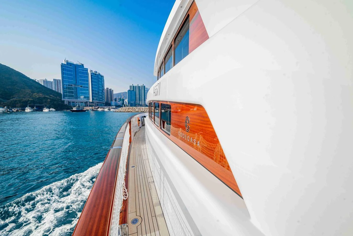 The yacht cruises smoothly along the coastline with a modern cityscape in the background. aboard VERO Yacht for Sale