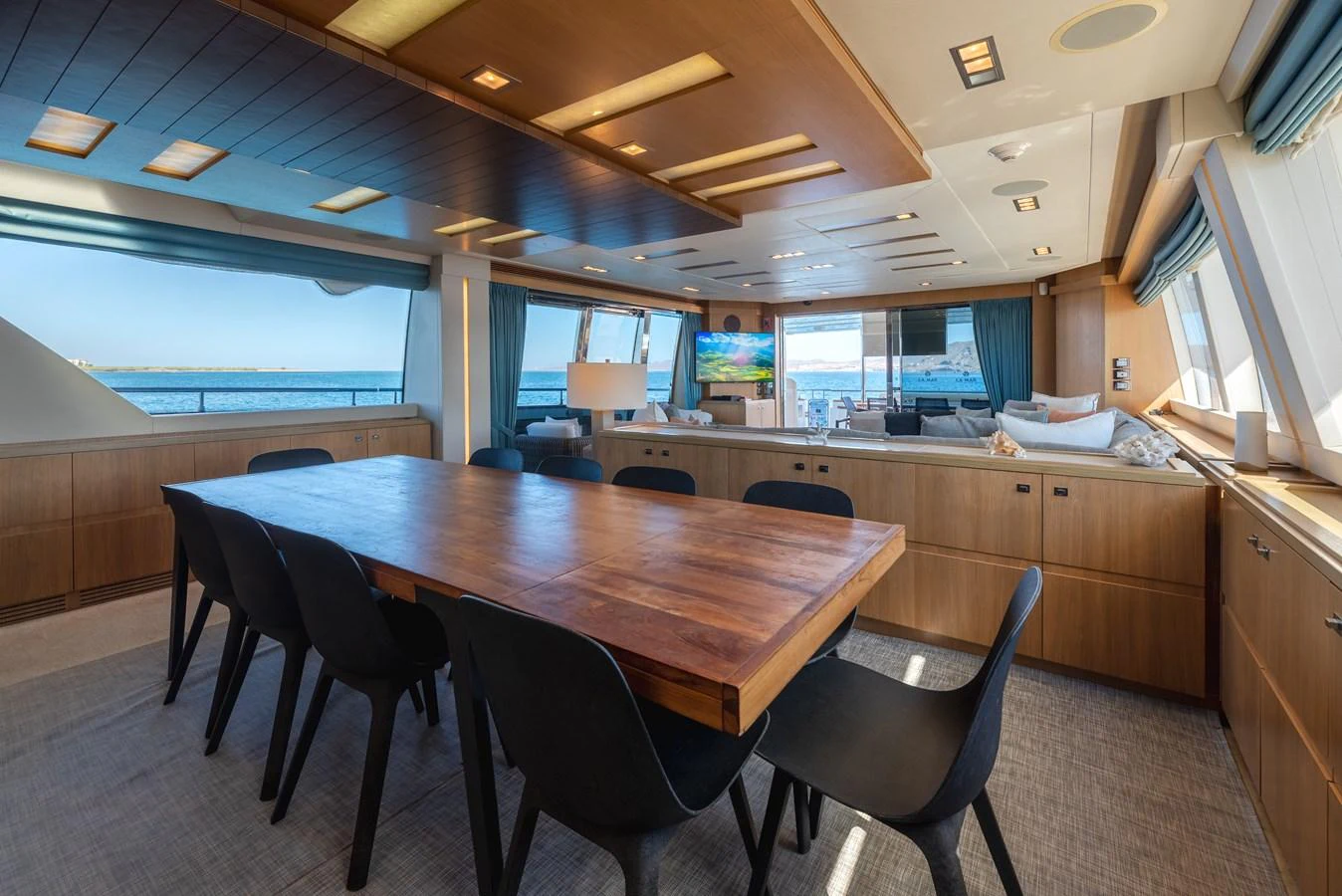 The yacht's dining area features a large wooden table surrounded by modern black chairs, with ample natural light streaming through large windows. aboard AMORE MIO Yacht for Sale