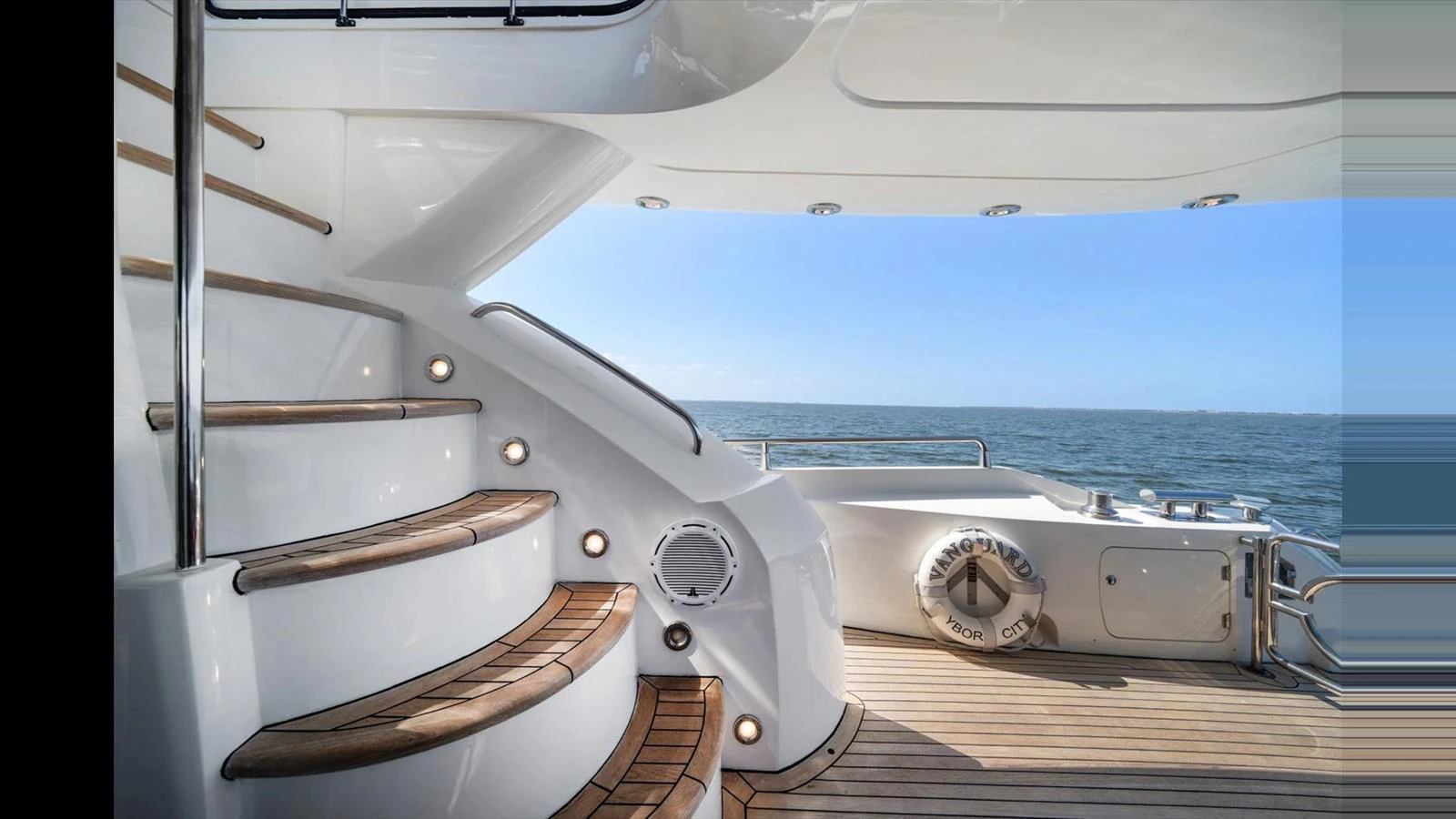 The aft deck features elegant wooden steps leading to an upper level, with a view of the open sea. aboard VANGUARD Yacht for Sale
