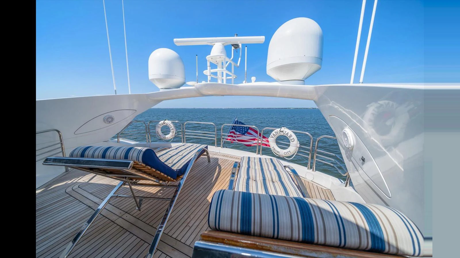 The sundeck offers a relaxing space with striped lounge chairs and a stunning view of the open sea. aboard VANGUARD Yacht for Sale