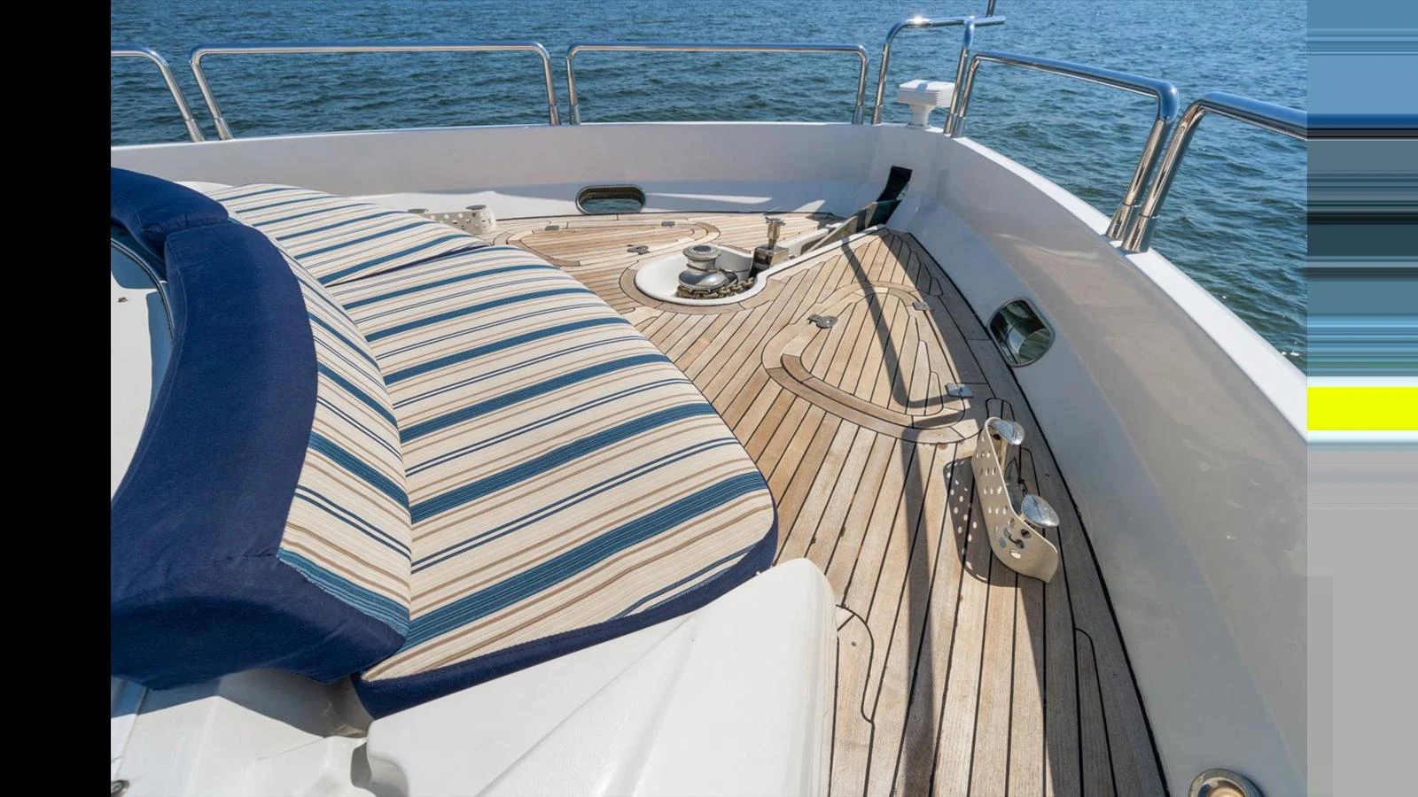 The foredeck features a comfortable sunpad with striped cushions and teak decking, perfect for relaxation. aboard VANGUARD Yacht for Sale