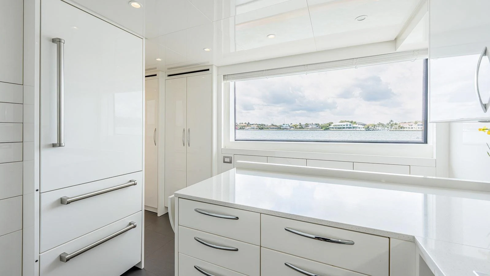 The yacht's galley features sleek white cabinetry and modern appliances with a large window offering a scenic view. aboard BETTY JANE Yacht for Sale