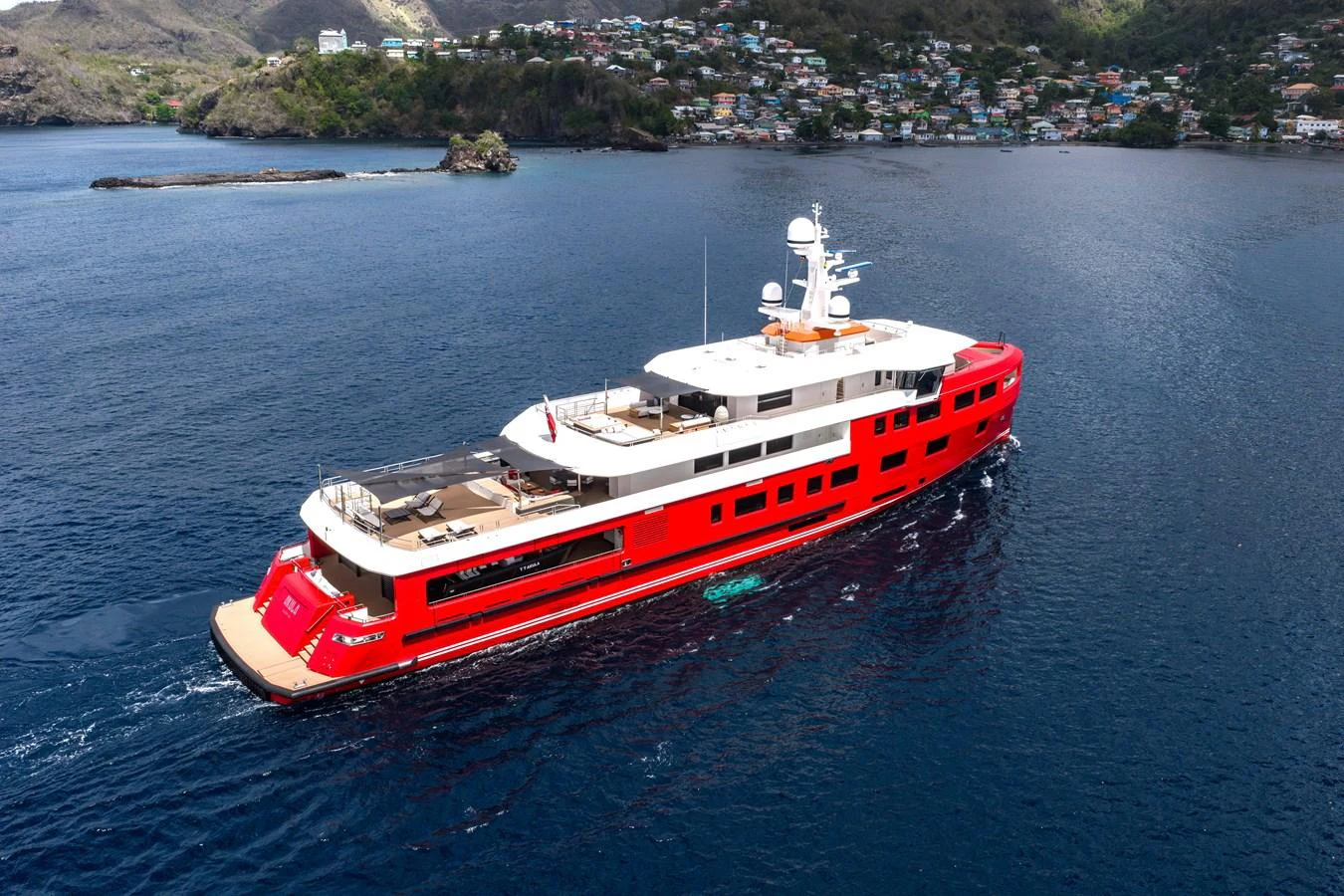 A striking red-hulled yacht cruises through serene blue waters with a scenic coastal backdrop. aboard AKULA Yacht for Sale