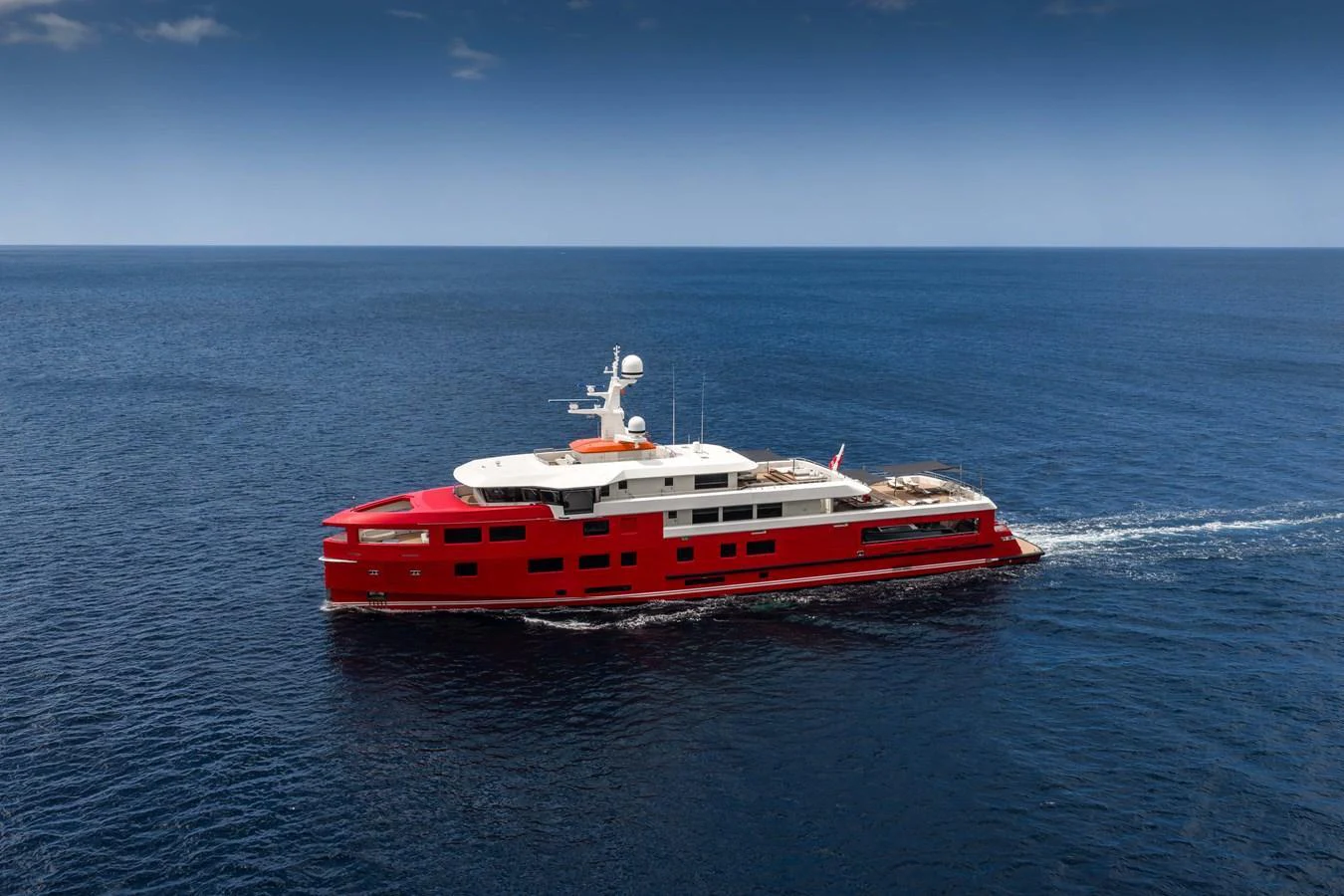 A striking red yacht cruises through calm blue waters under a clear sky. aboard AKULA Yacht for Sale