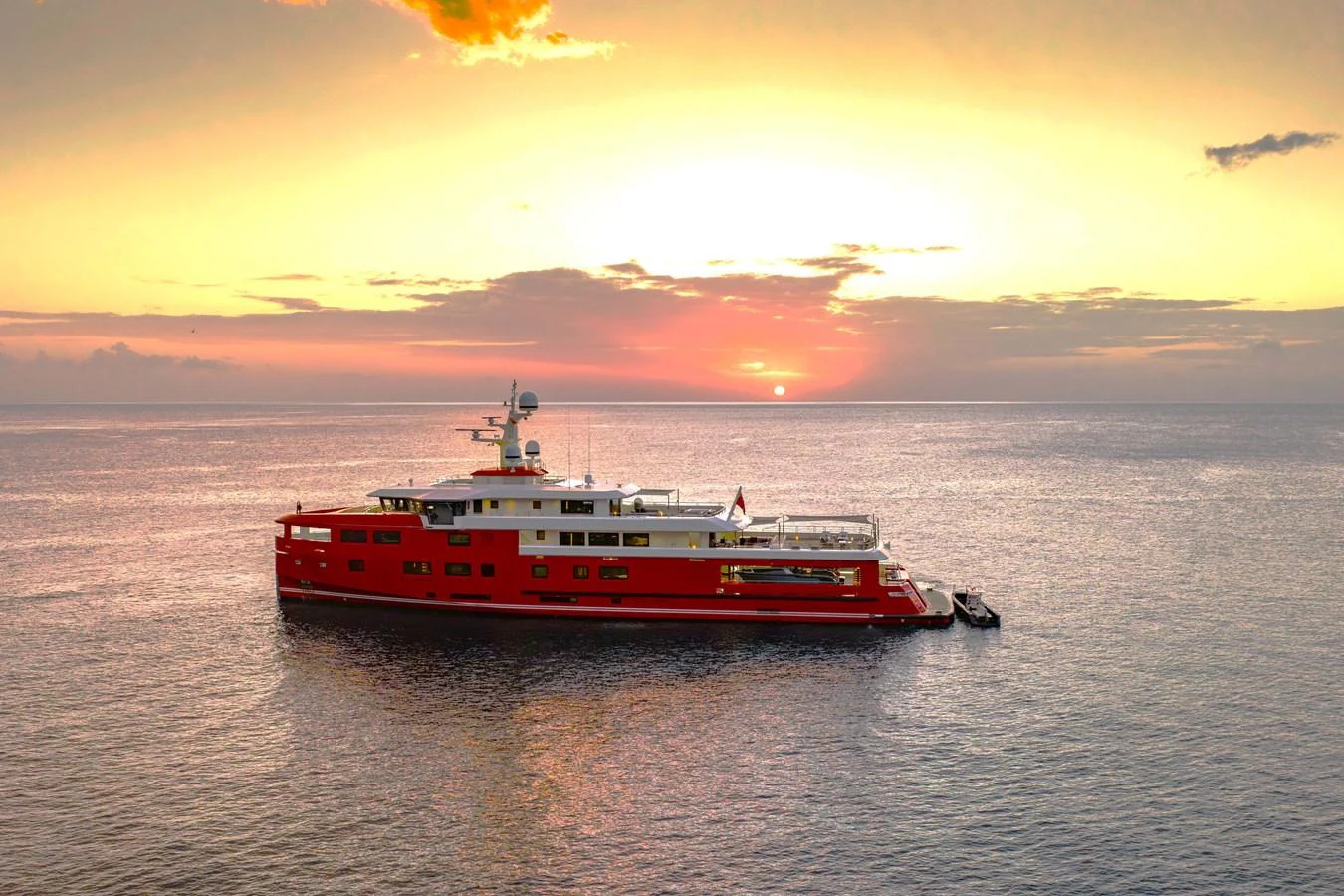 A striking red yacht is anchored on calm waters at sunset, creating a picturesque scene. aboard AKULA Yacht for Sale