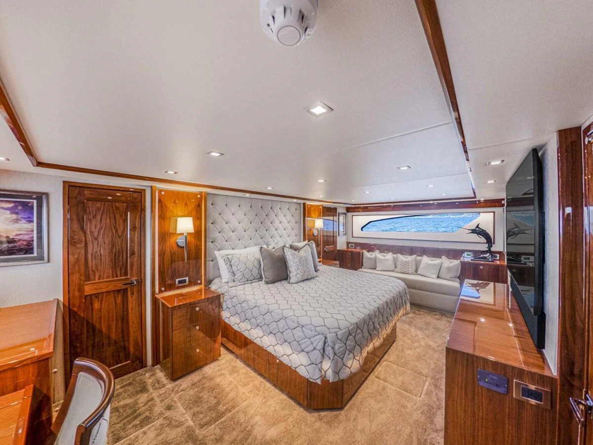 The master stateroom features a luxurious bed, elegant wood finishes, and a large window with a scenic view. aboard MARLIN MAGIC Yacht for Sale
