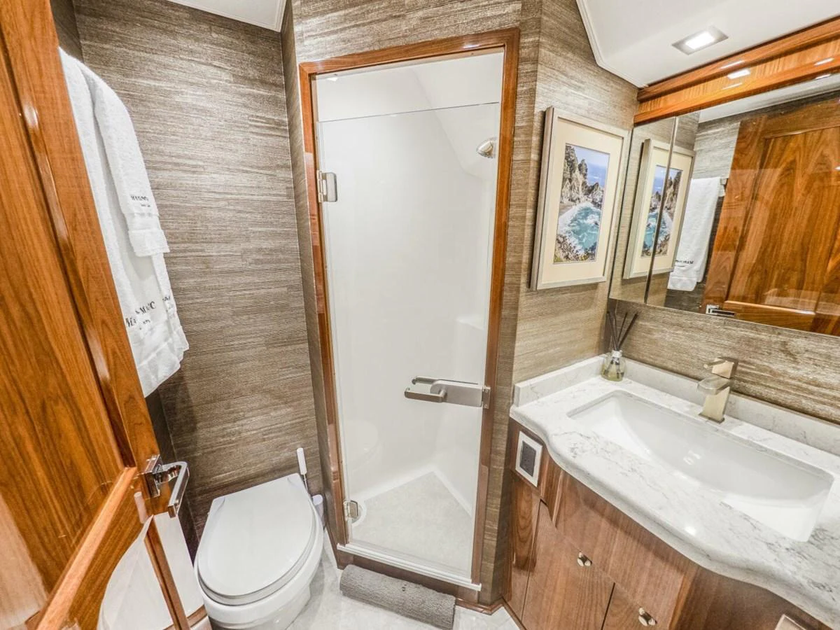 A luxurious yacht bathroom featuring a glass-enclosed shower, elegant wood finishes, and a marble countertop. aboard MARLIN MAGIC Yacht for Sale