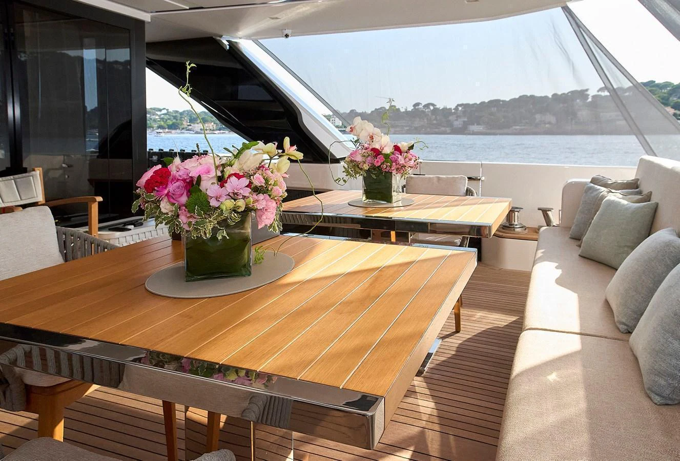 The aft deck features elegant dining tables adorned with fresh floral arrangements, offering a serene view of the water. aboard SANLORENZO SL102 ASYMMETRIC Yacht for Sale