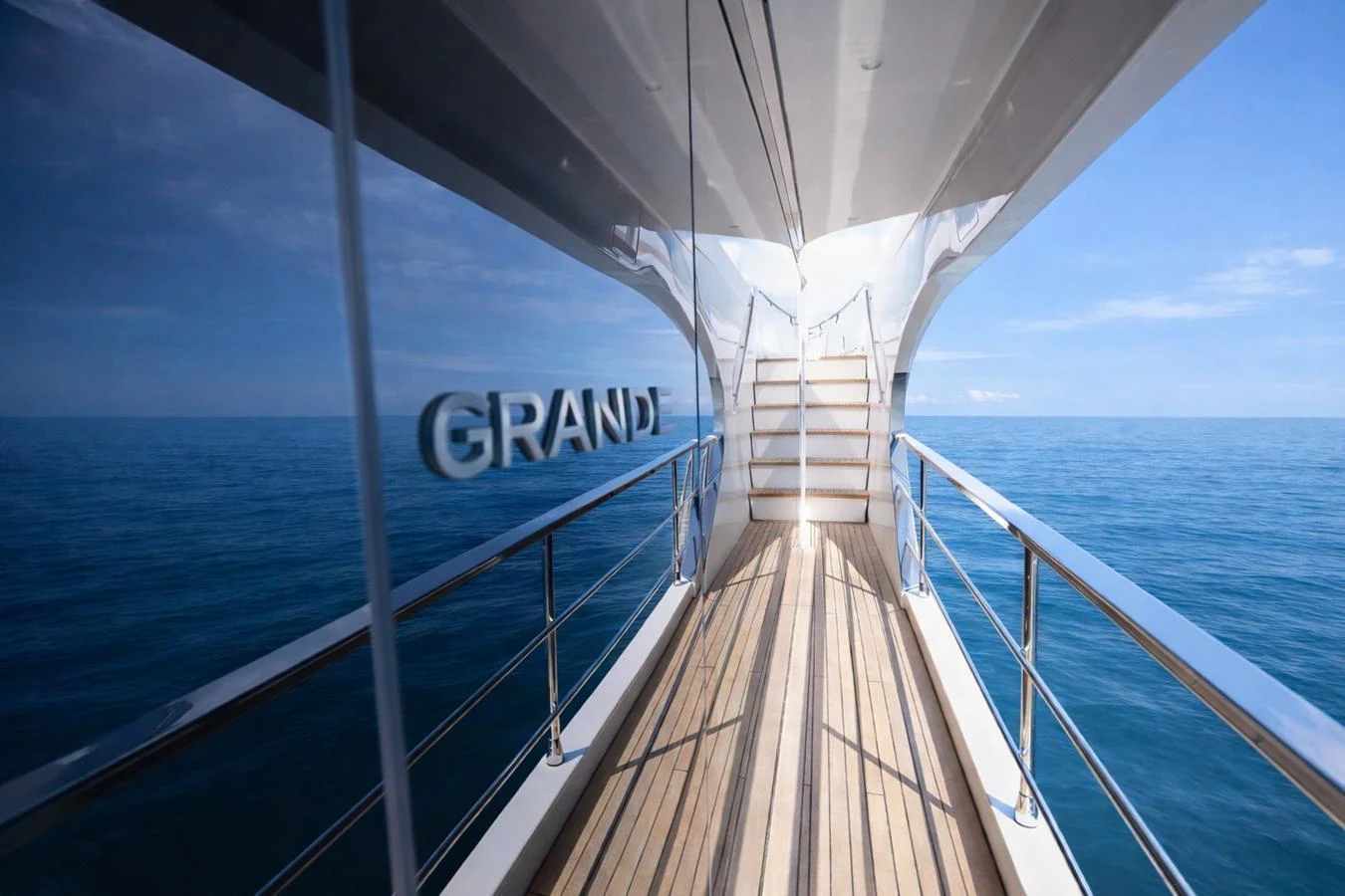 A sleek yacht walkway with wooden decking and stainless steel railings, leading to an upper deck under a clear blue sky. aboard SEA STAR Yacht for Sale