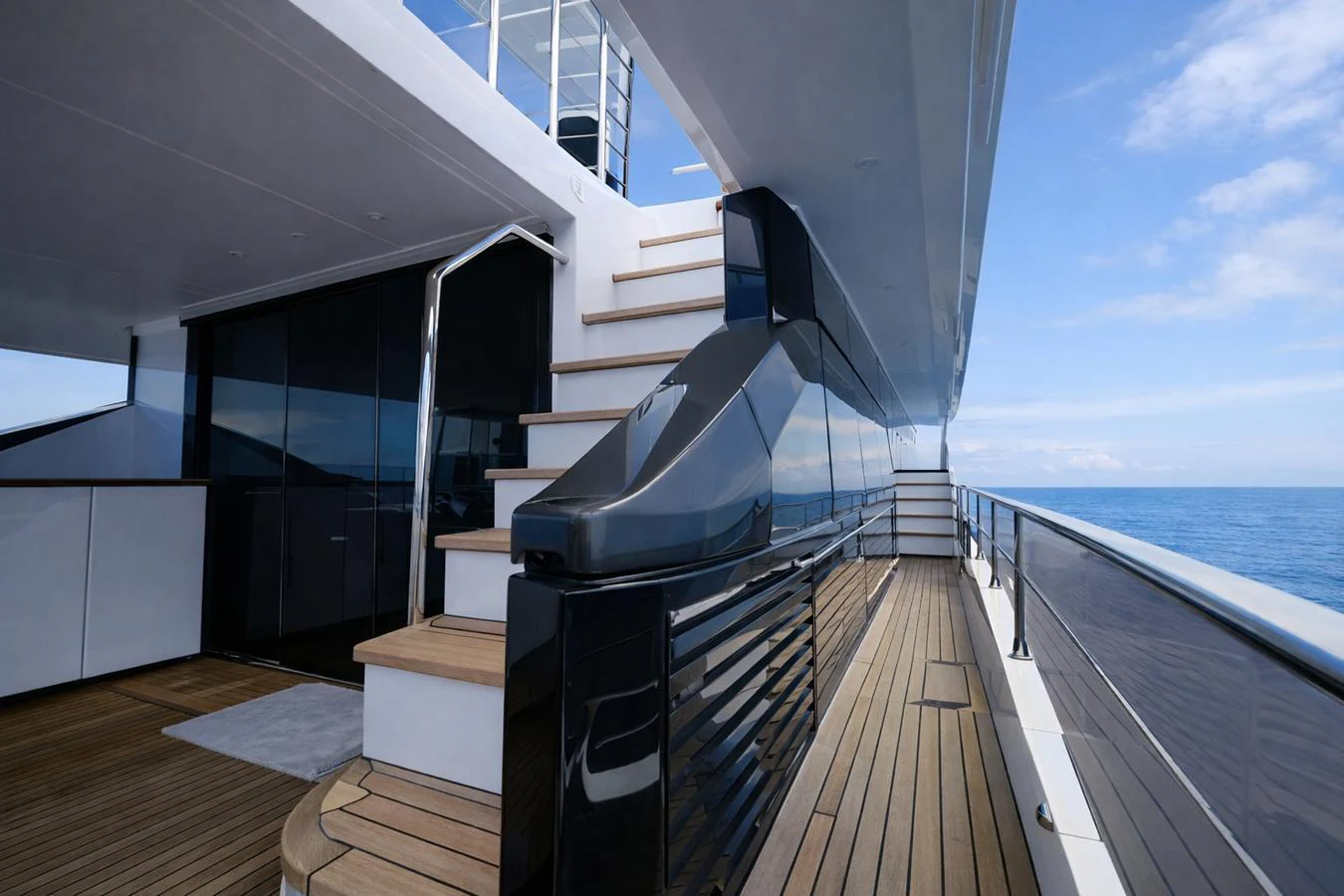 The sleek side deck of the yacht features polished wood steps and modern railings, leading to an upper level with panoramic ocean views. aboard SEA STAR Yacht for Sale