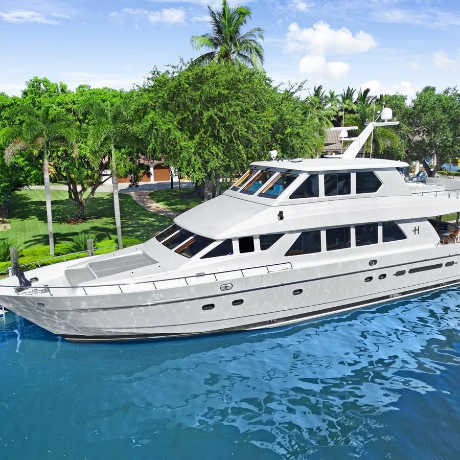 A sleek and elegant yacht is docked in a serene, tropical setting with lush greenery and clear blue water. aboard MILES AWEIGH Yacht for Sale