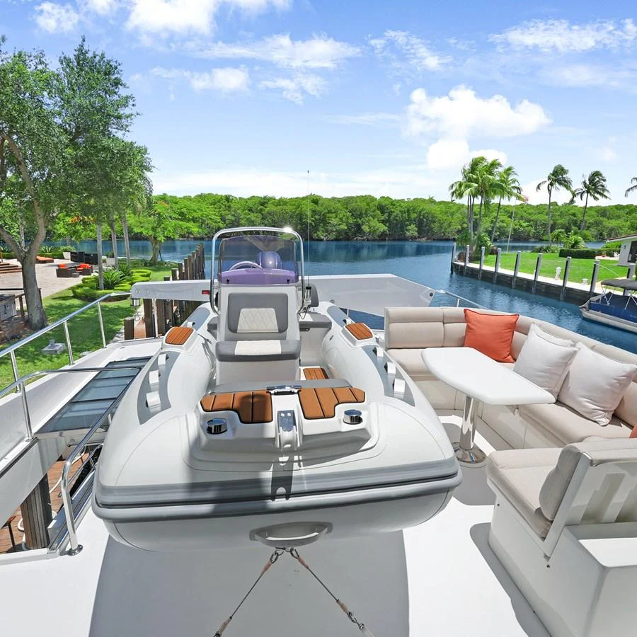A sleek tender is positioned on the deck, surrounded by comfortable seating and lush greenery in the background. aboard MILES AWEIGH Yacht for Sale