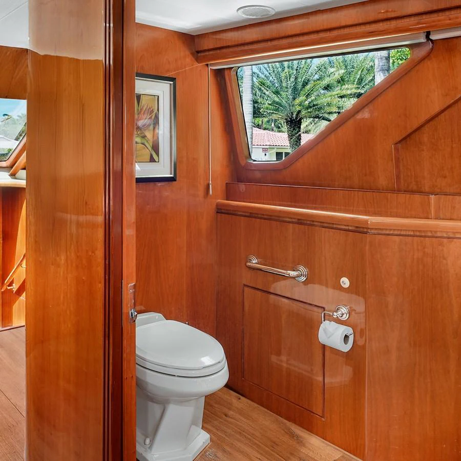 The yacht's head features warm wood paneling and a window with a view of palm trees. aboard MILES AWEIGH Yacht for Sale