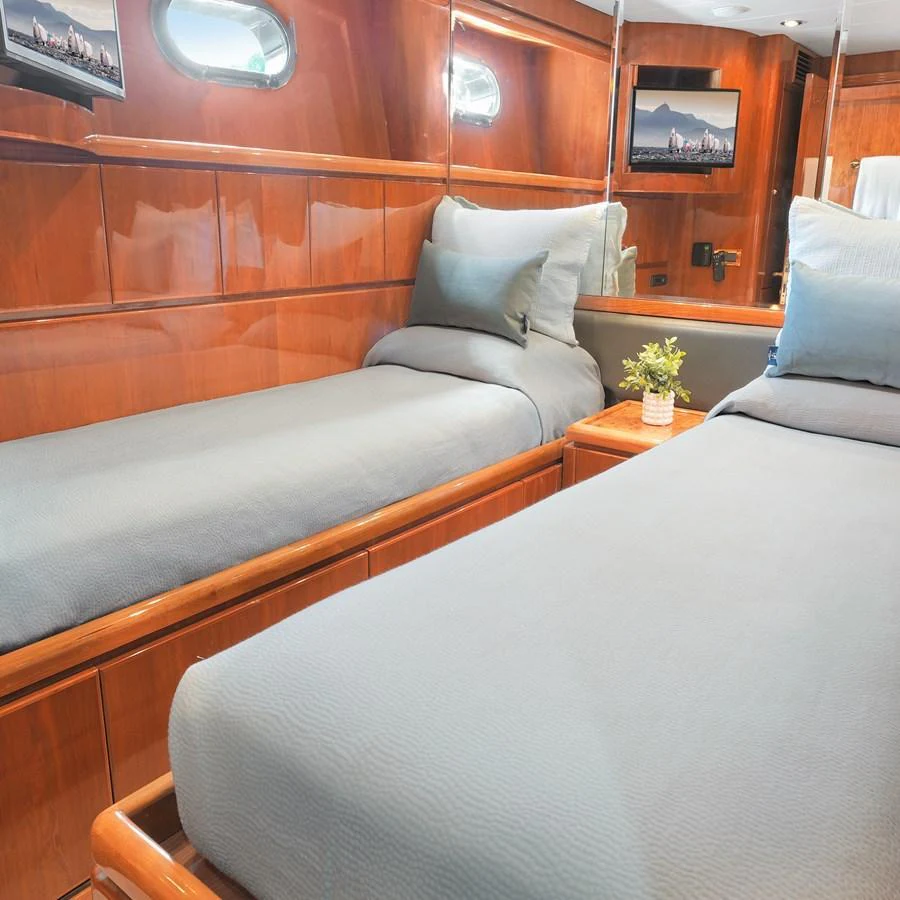 The twin stateroom features cozy beds with elegant wood paneling and a mirrored wall for a spacious feel. aboard MILES AWEIGH Yacht for Sale