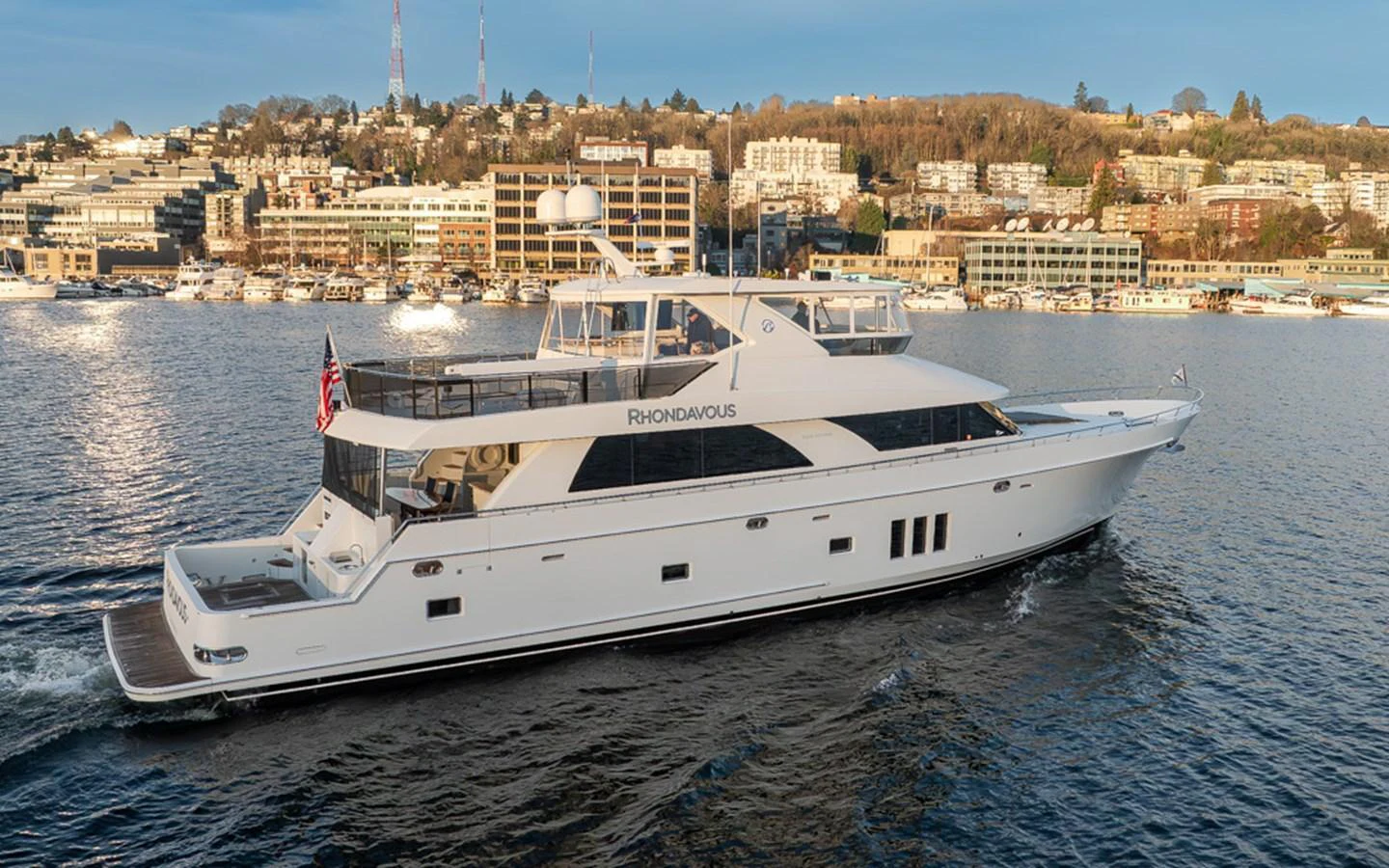 A sleek and elegant yacht cruises through the water with a cityscape in the background. aboard RHONDAVOUS Yacht for Sale