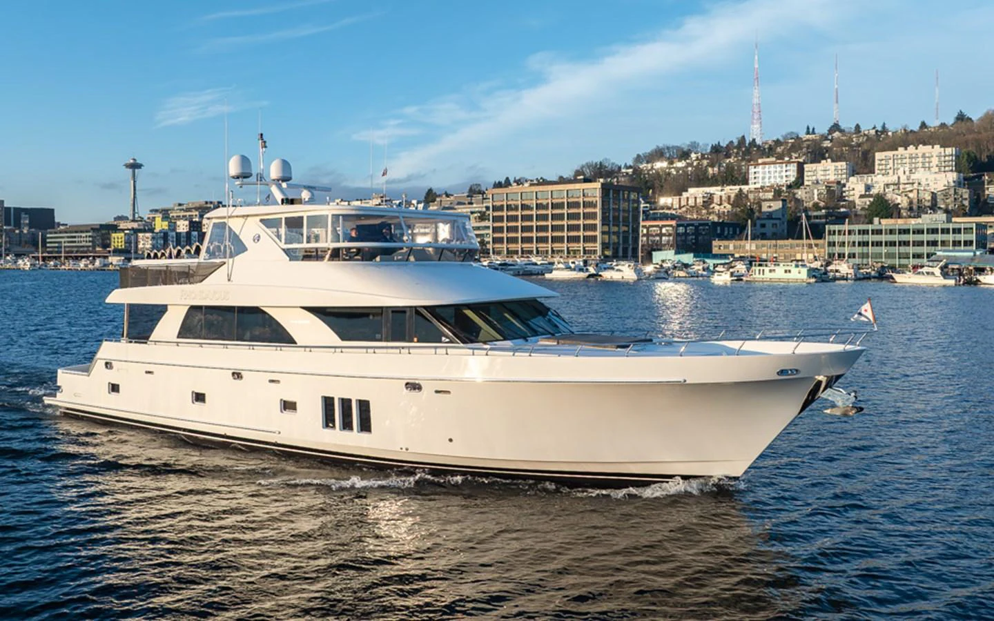 A sleek and modern yacht cruises gracefully on a calm body of water with a cityscape in the background. aboard RHONDAVOUS Yacht for Sale