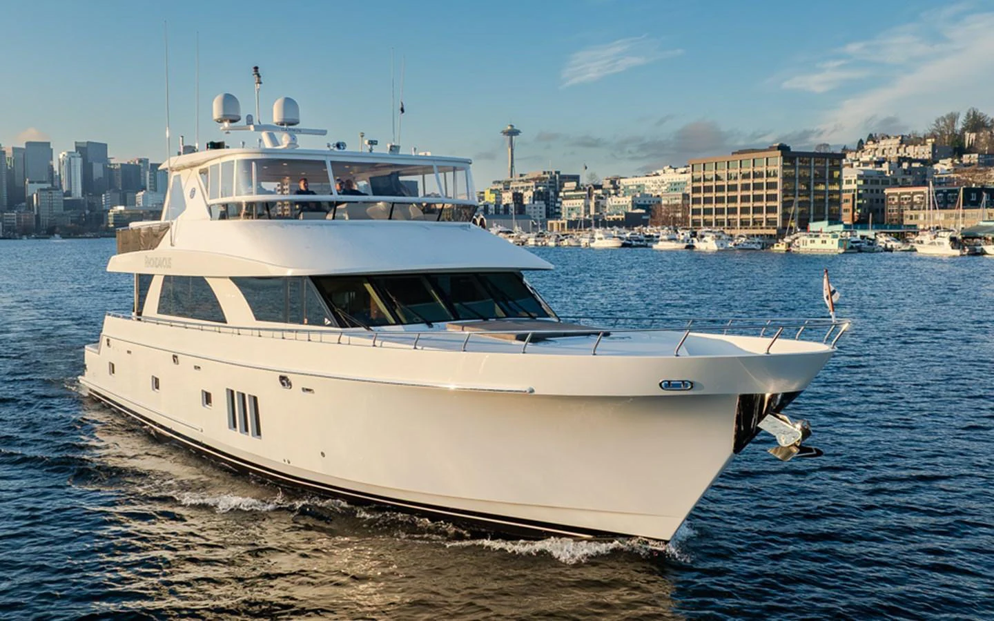 A sleek and modern yacht cruises through the water with a cityscape in the background. aboard RHONDAVOUS Yacht for Sale