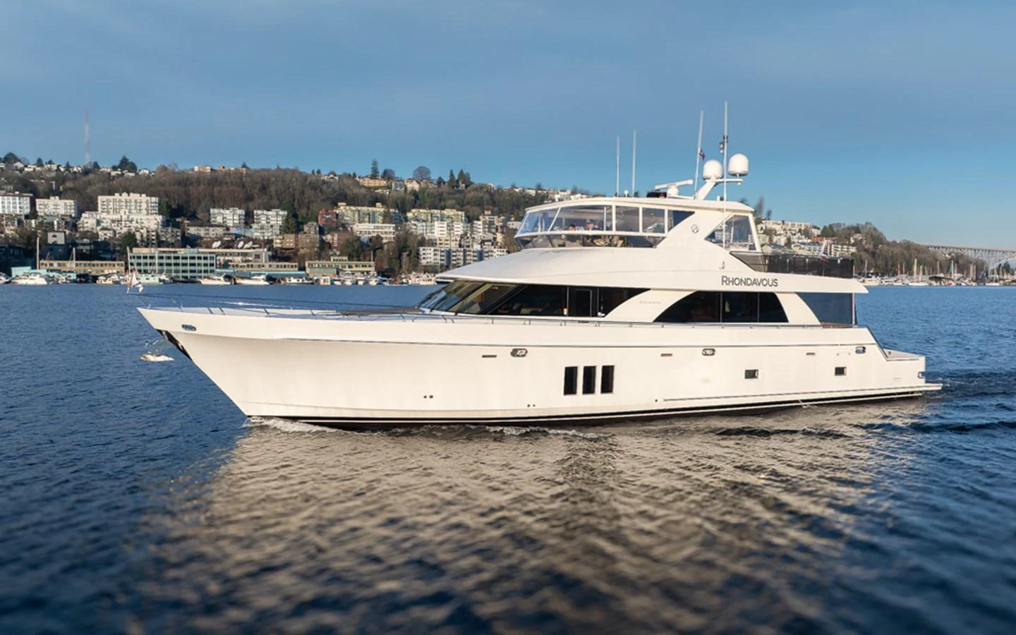 A sleek and modern yacht cruises gracefully on calm waters with a scenic shoreline in the background. aboard RHONDAVOUS Yacht for Sale