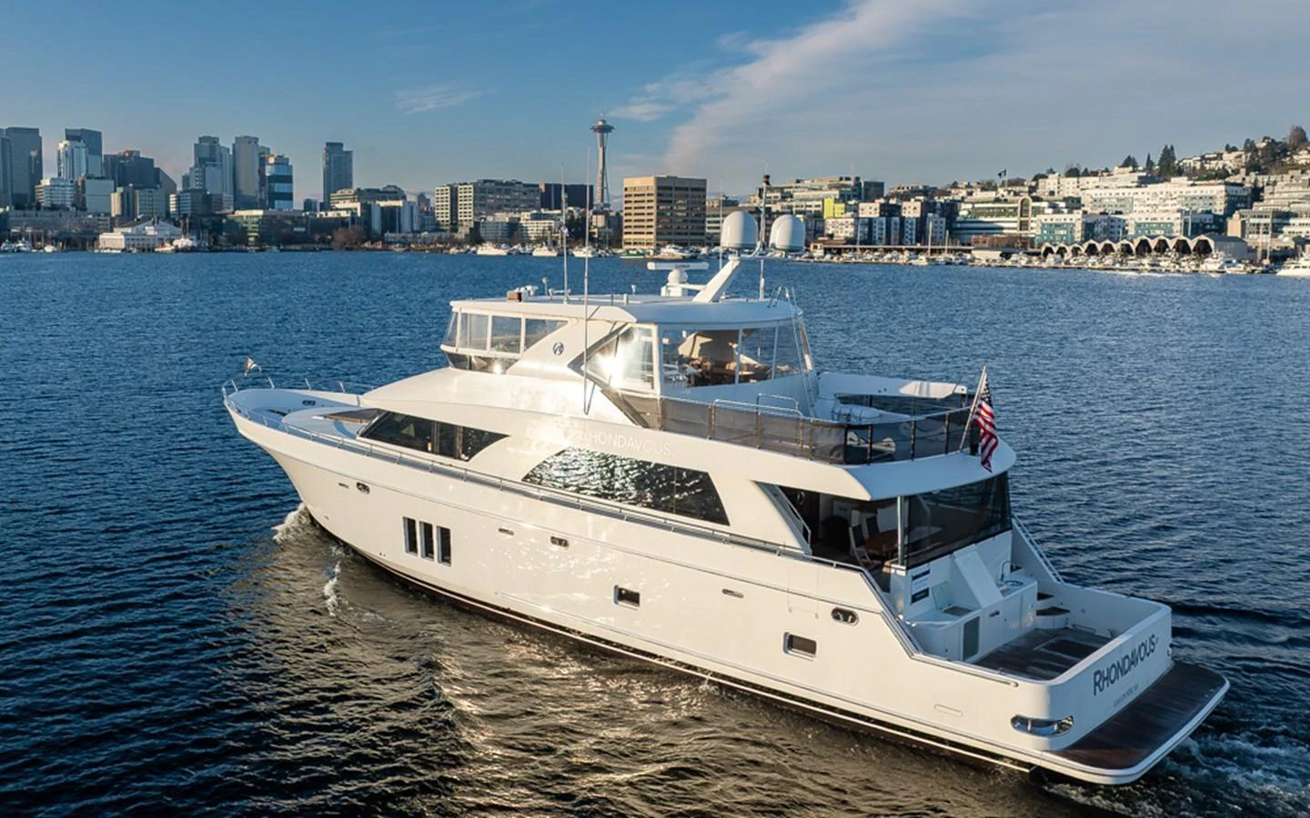 A sleek and modern yacht cruises gracefully on calm waters with a cityscape in the background. aboard RHONDAVOUS Yacht for Sale