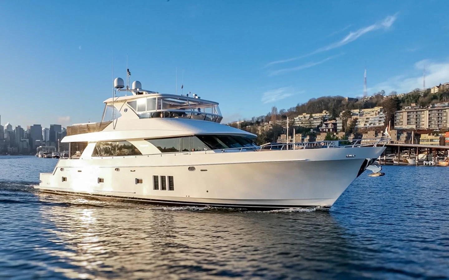 A sleek and modern yacht cruises gracefully on calm waters with a cityscape in the background. aboard RHONDAVOUS Yacht for Sale