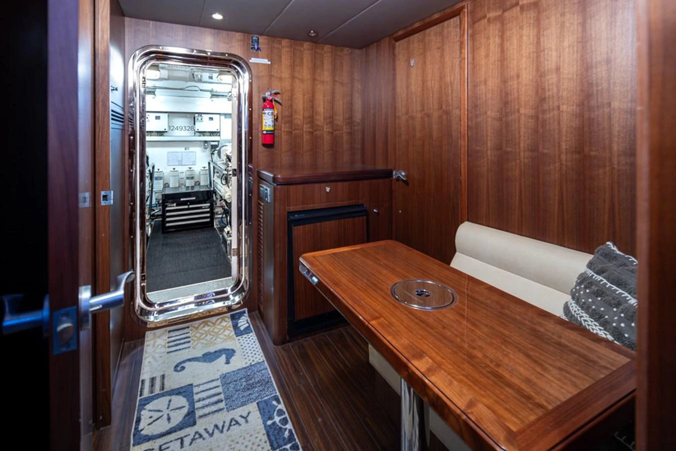 The image showcases a cozy crew area with a wooden table, seating, and access to the engine room. aboard RHONDAVOUS Yacht for Sale