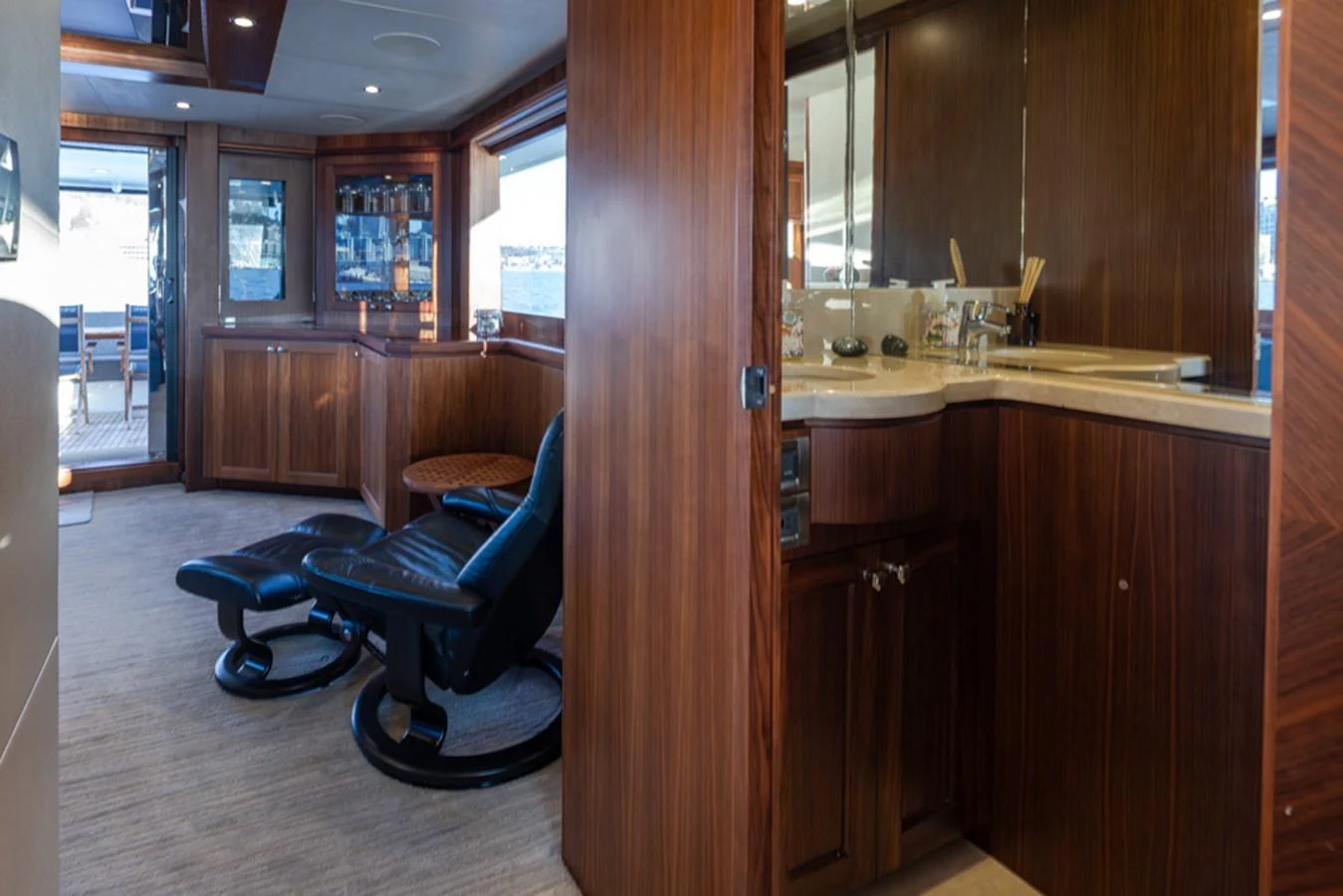 The yacht's interior features a cozy seating area with a luxurious chair and ottoman, complemented by rich wooden cabinetry and a well-appointed vanity. aboard RHONDAVOUS Yacht for Sale
