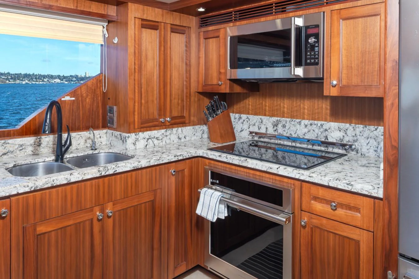 The yacht's galley features rich wooden cabinetry, modern appliances, and a scenic view through the window. aboard RHONDAVOUS Yacht for Sale