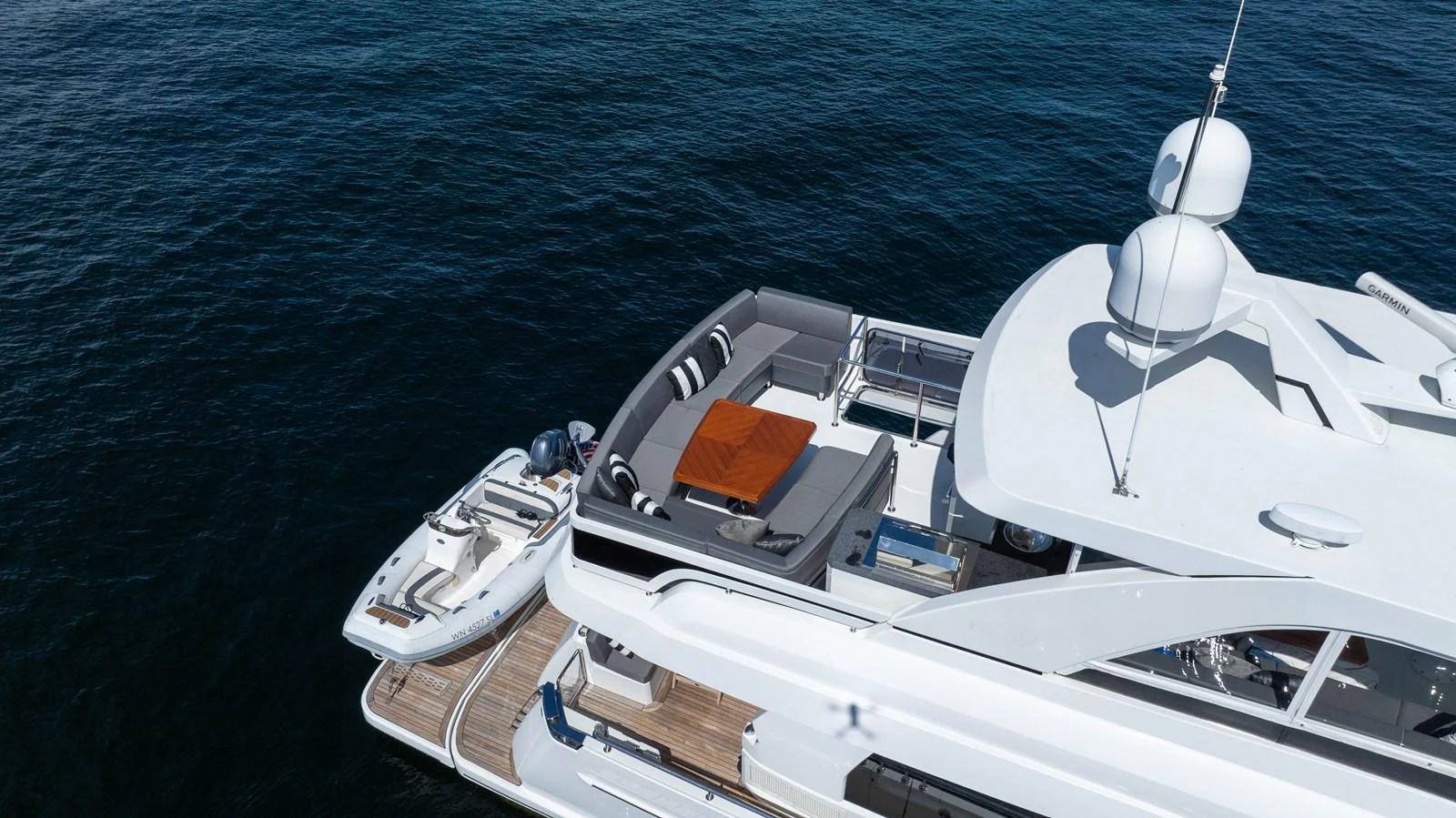 The yacht's aft deck features a luxurious lounging area with a tender docked alongside. aboard SUB-PAR Yacht for Sale