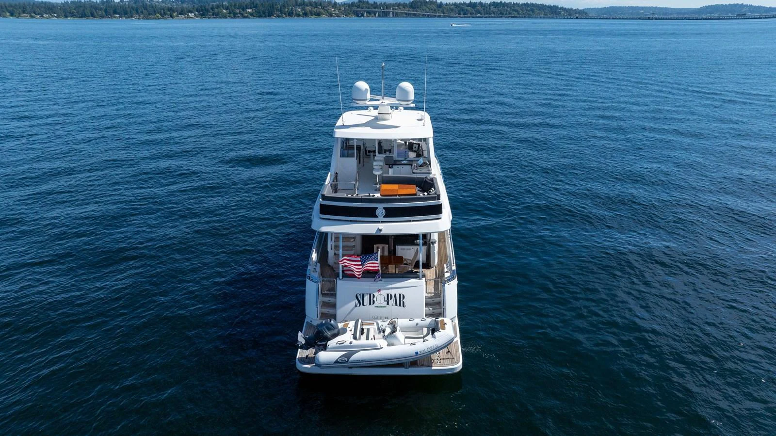 A yacht is seen from the rear, cruising on calm waters with a scenic backdrop. aboard SUB-PAR Yacht for Sale