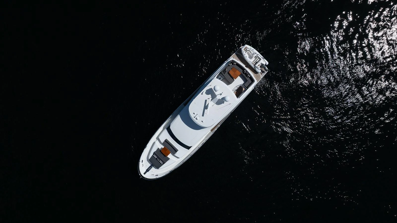 A sleek yacht glides gracefully over dark, shimmering waters, showcasing its elegant design from an aerial perspective. aboard SUB-PAR Yacht for Sale