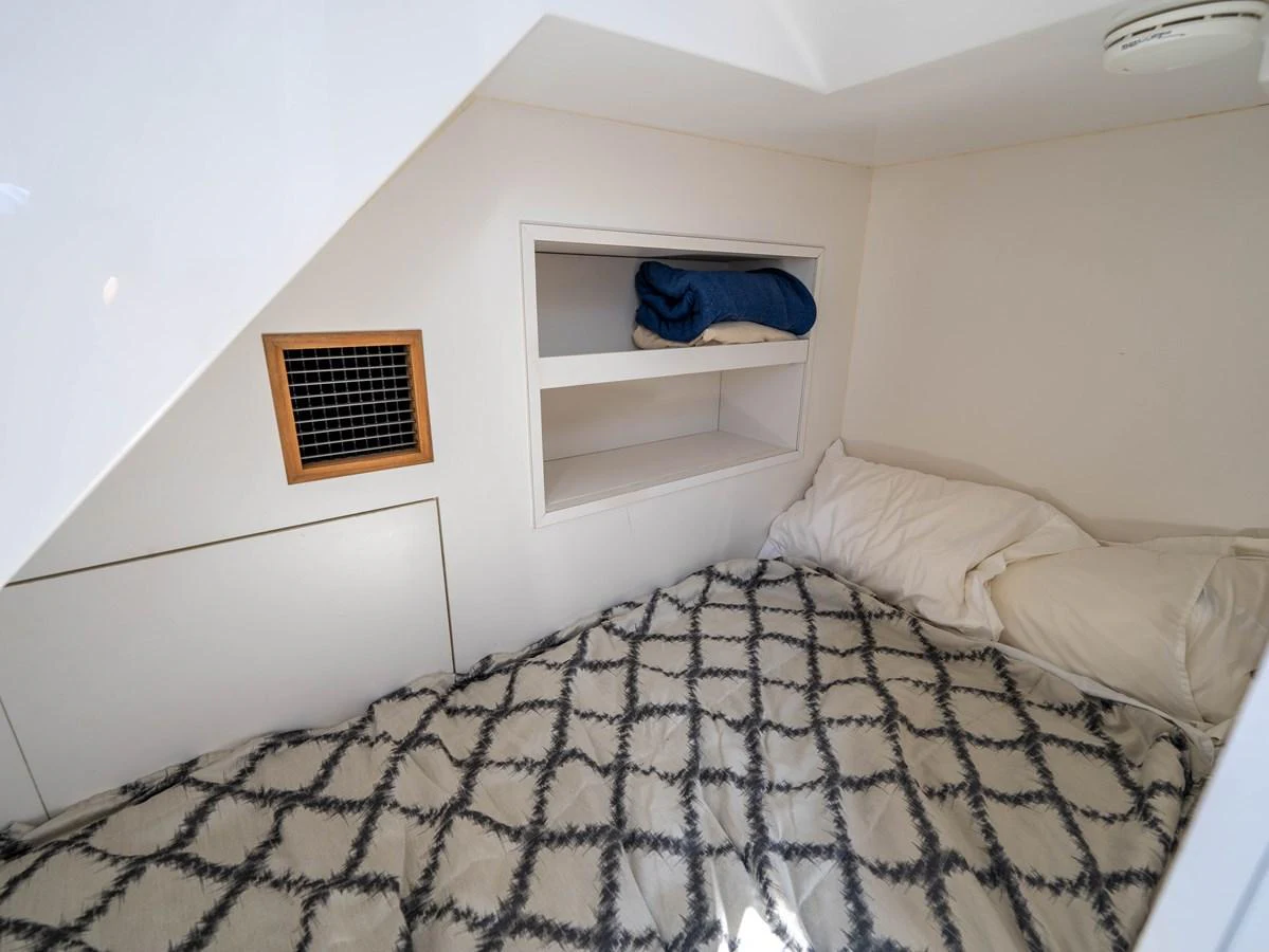 A cozy cabin with a neatly made bed and storage shelves. aboard SUB-PAR Yacht for Sale