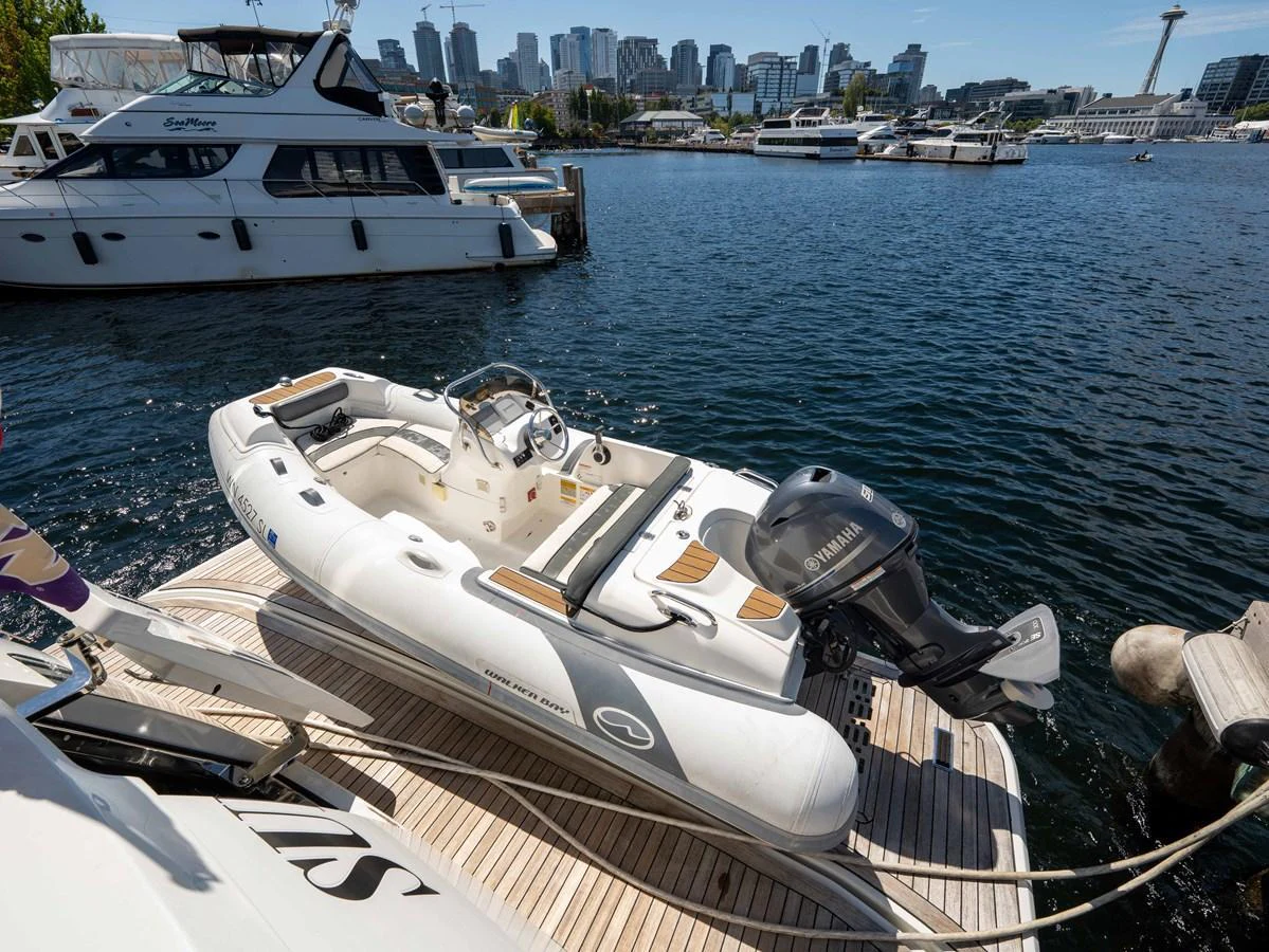 A sleek tender boat is docked on the yacht's swim platform with a city skyline in the background. aboard SUB-PAR Yacht for Sale