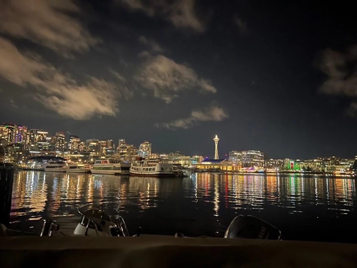 A serene night view of yachts docked in a vibrant city marina with illuminated skyline. aboard SUB-PAR Yacht for Sale