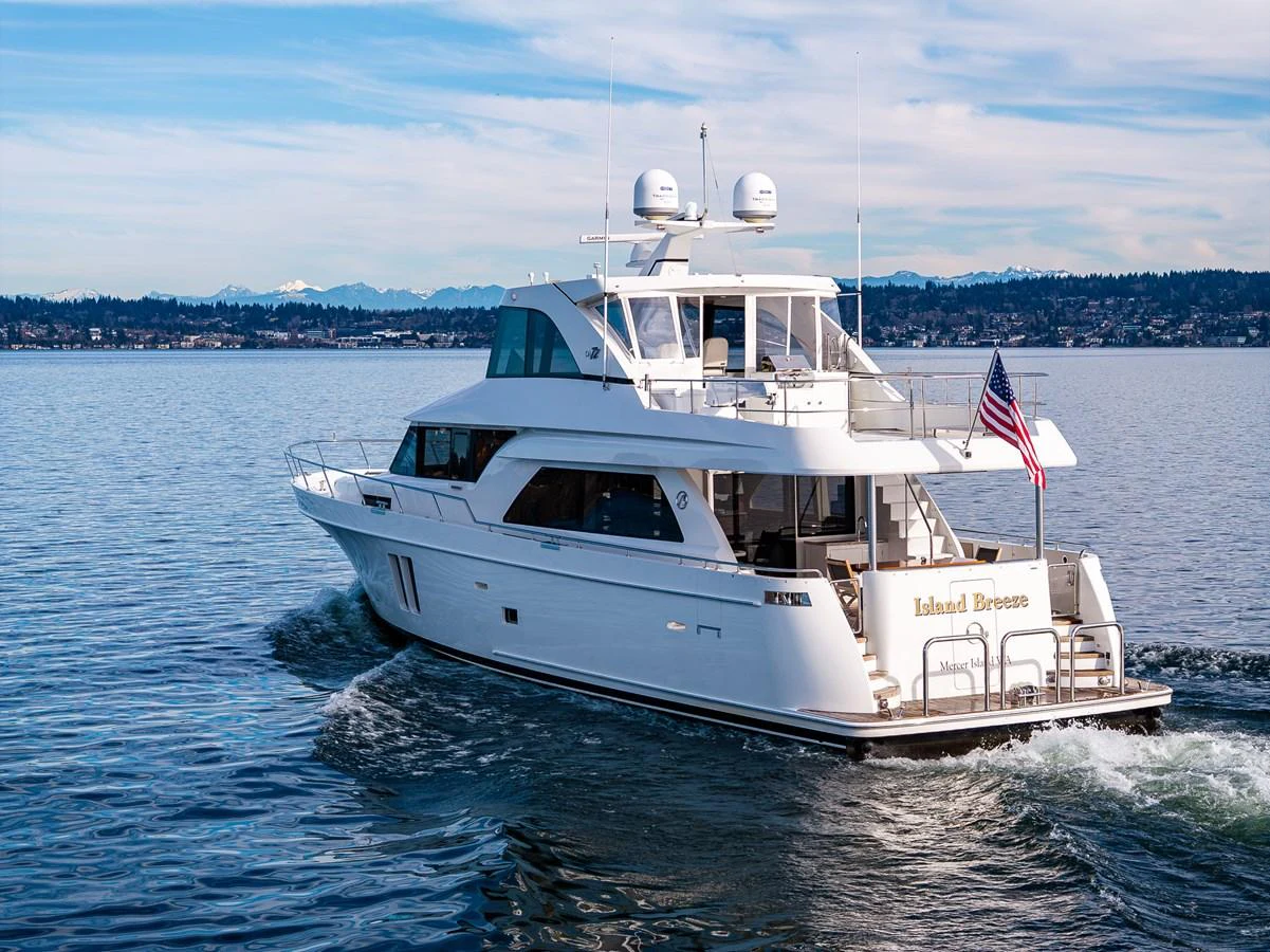 A pristine yacht cruises smoothly on calm waters with a scenic shoreline in the background. aboard ISLAND BREEZE Yacht for Sale
