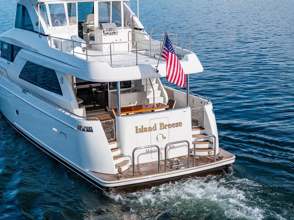 The yacht's aft deck is beautifully showcased as it cruises through calm waters, featuring an inviting seating area and an American flag. aboard ISLAND BREEZE Yacht for Sale