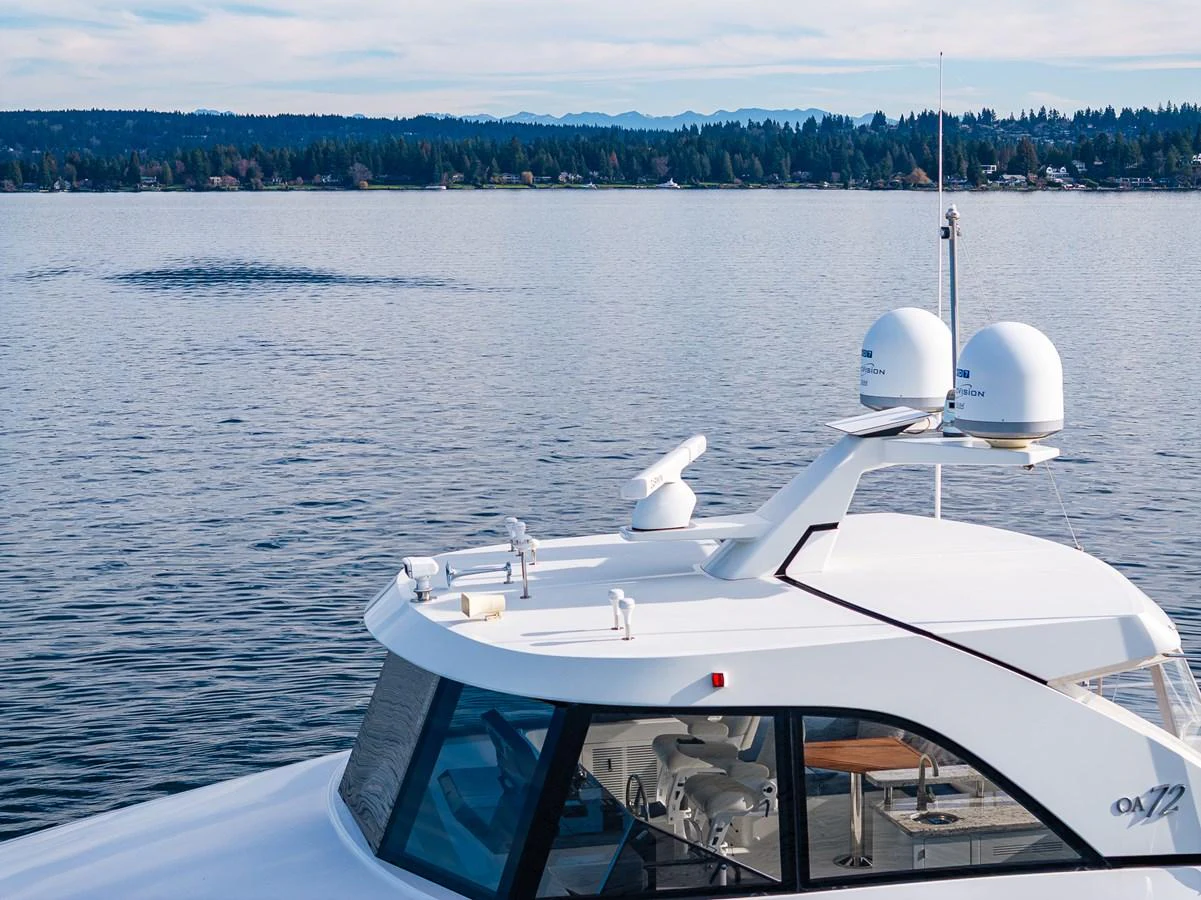 A sleek yacht with modern radar equipment cruises on a calm lake with a scenic forested shoreline in the background. aboard ISLAND BREEZE Yacht for Sale